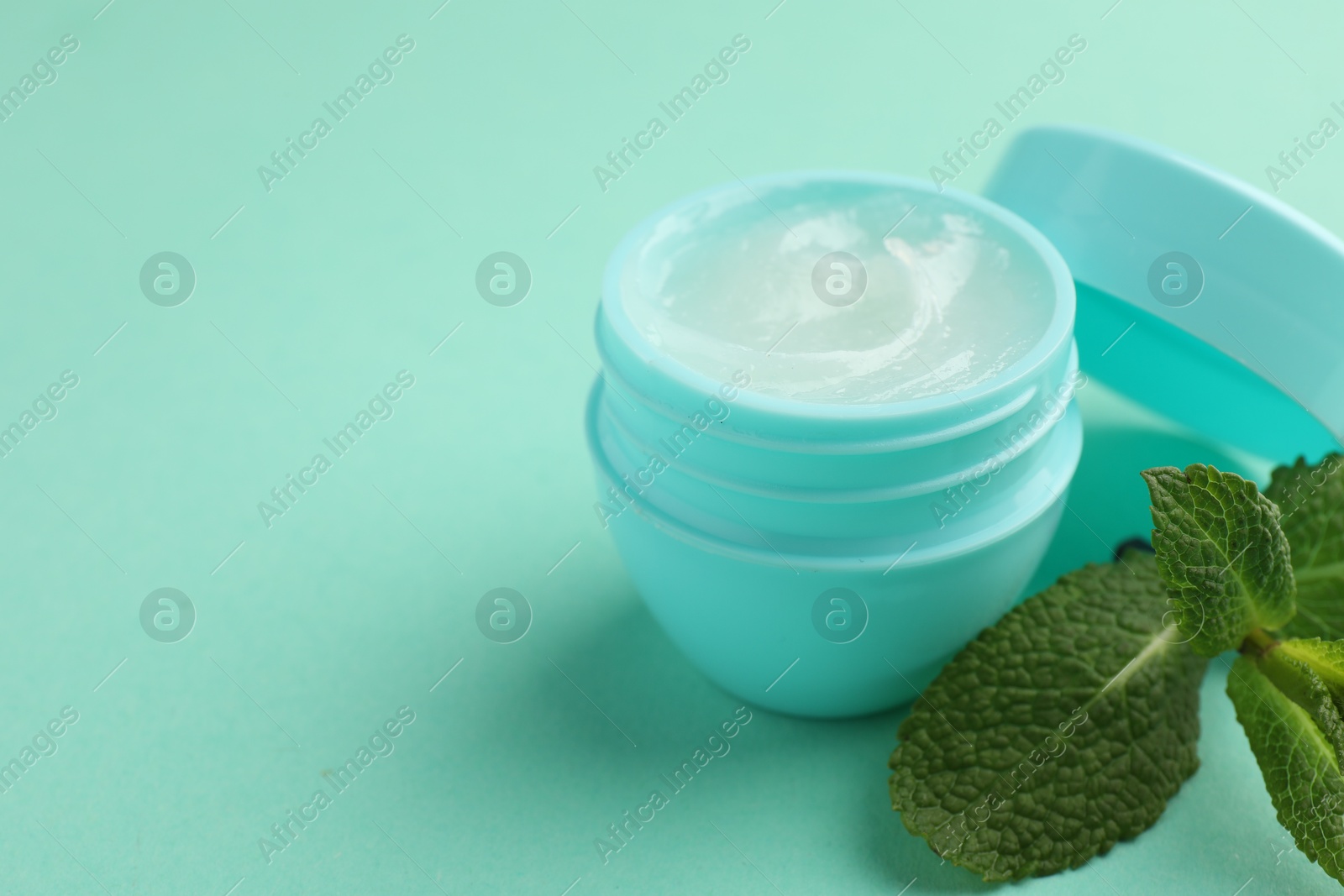 Photo of Natural lip balm and mint leaves on turquoise background, closeup. Space for text