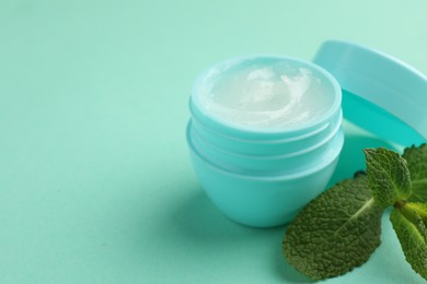 Photo of Natural lip balm and mint leaves on turquoise background, closeup. Space for text