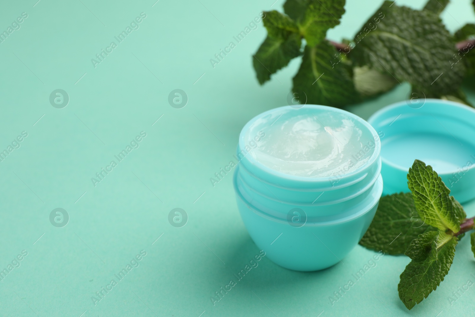 Photo of Natural lip balm and mint leaves on turquoise background, closeup. Space for text