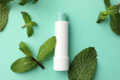 Photo of Natural lip balm and mint leaves on turquoise background, flat lay