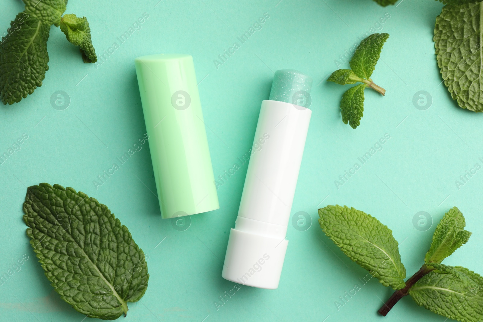 Photo of Natural lip balm and mint leaves on turquoise background, flat lay