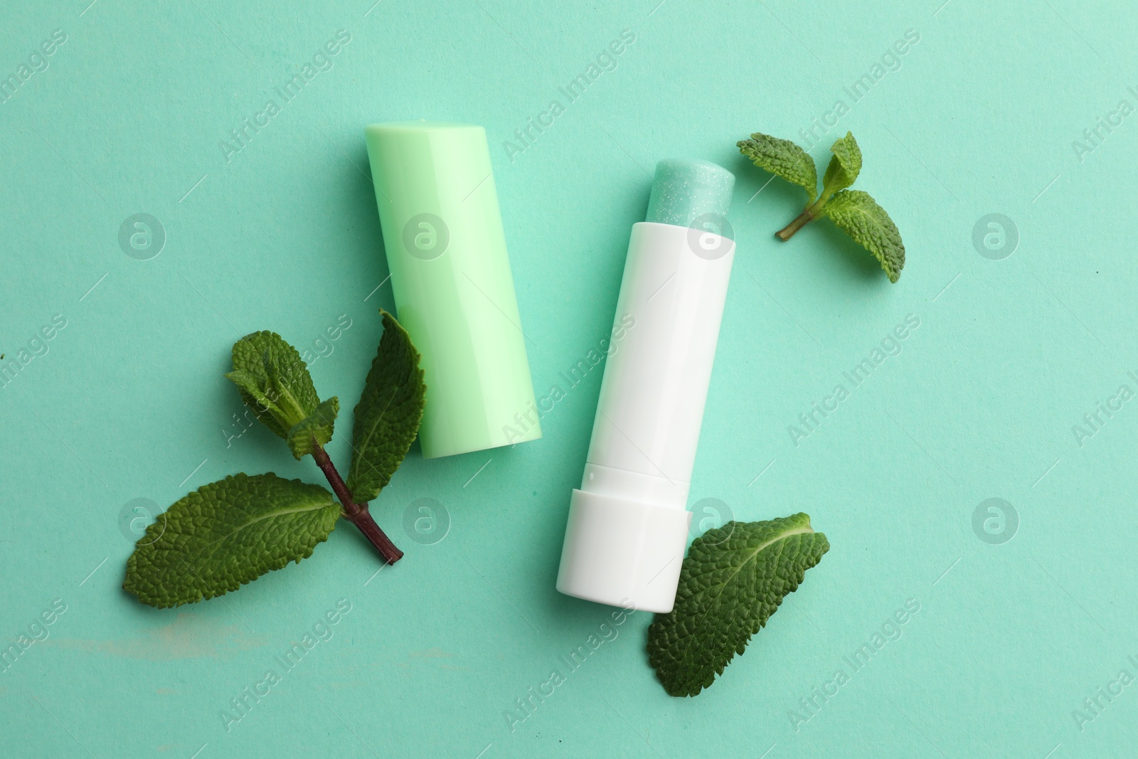 Photo of Natural lip balm and mint leaves on turquoise background, flat lay