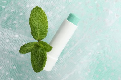 Photo of Natural lip balm, mint leaves and fabric on turquoise background, closeup