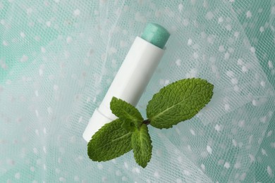 Photo of Natural lip balm, mint leaves and fabric on turquoise background, closeup