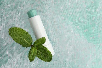 Photo of Natural lip balm, mint leaves and fabric on turquoise background, closeup. Space for text