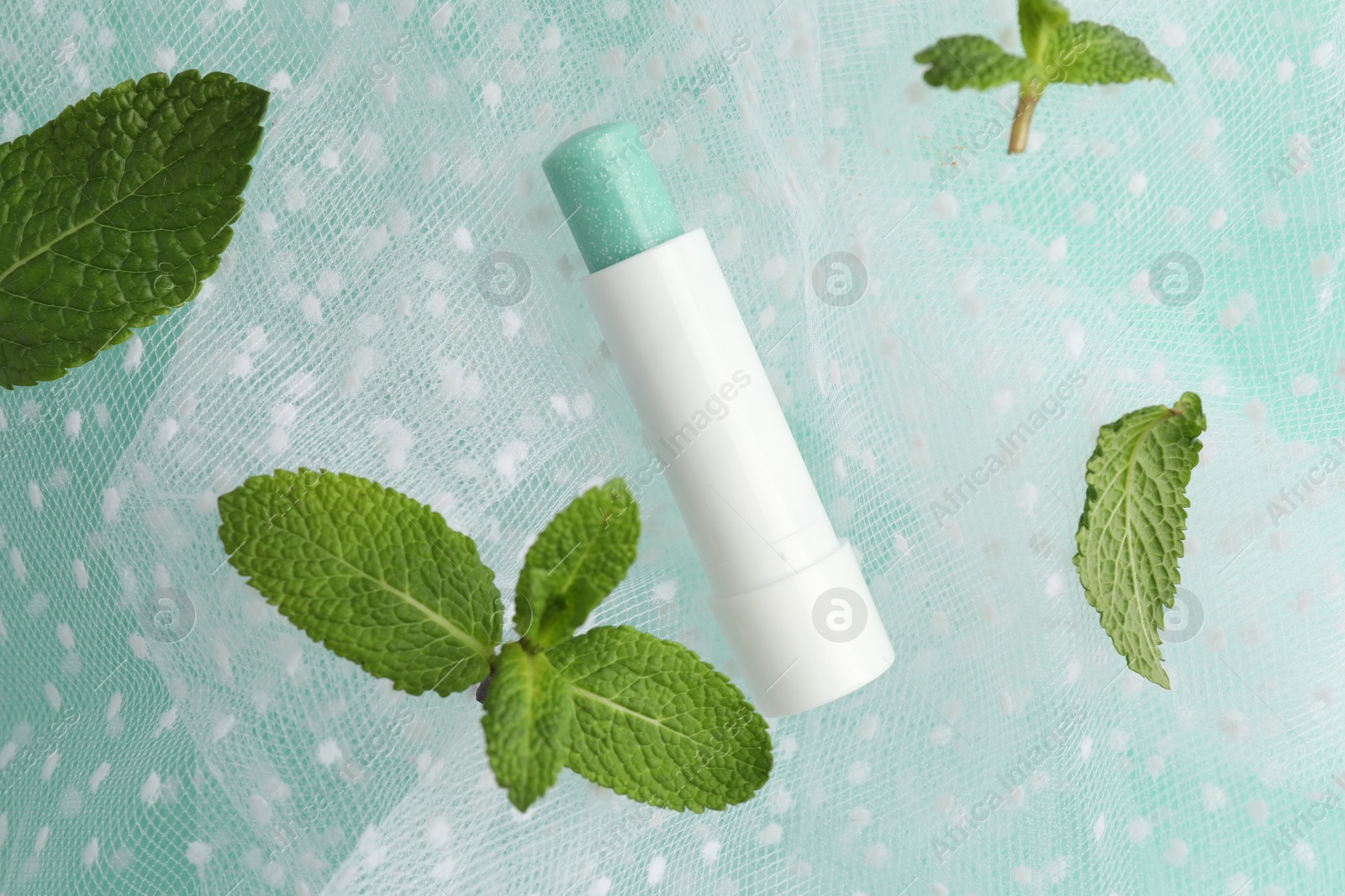 Photo of Natural lip balm, mint leaves and fabric on turquoise background, closeup