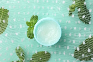 Photo of Natural lip balm, mint leaves and fabric on turquoise background, top view