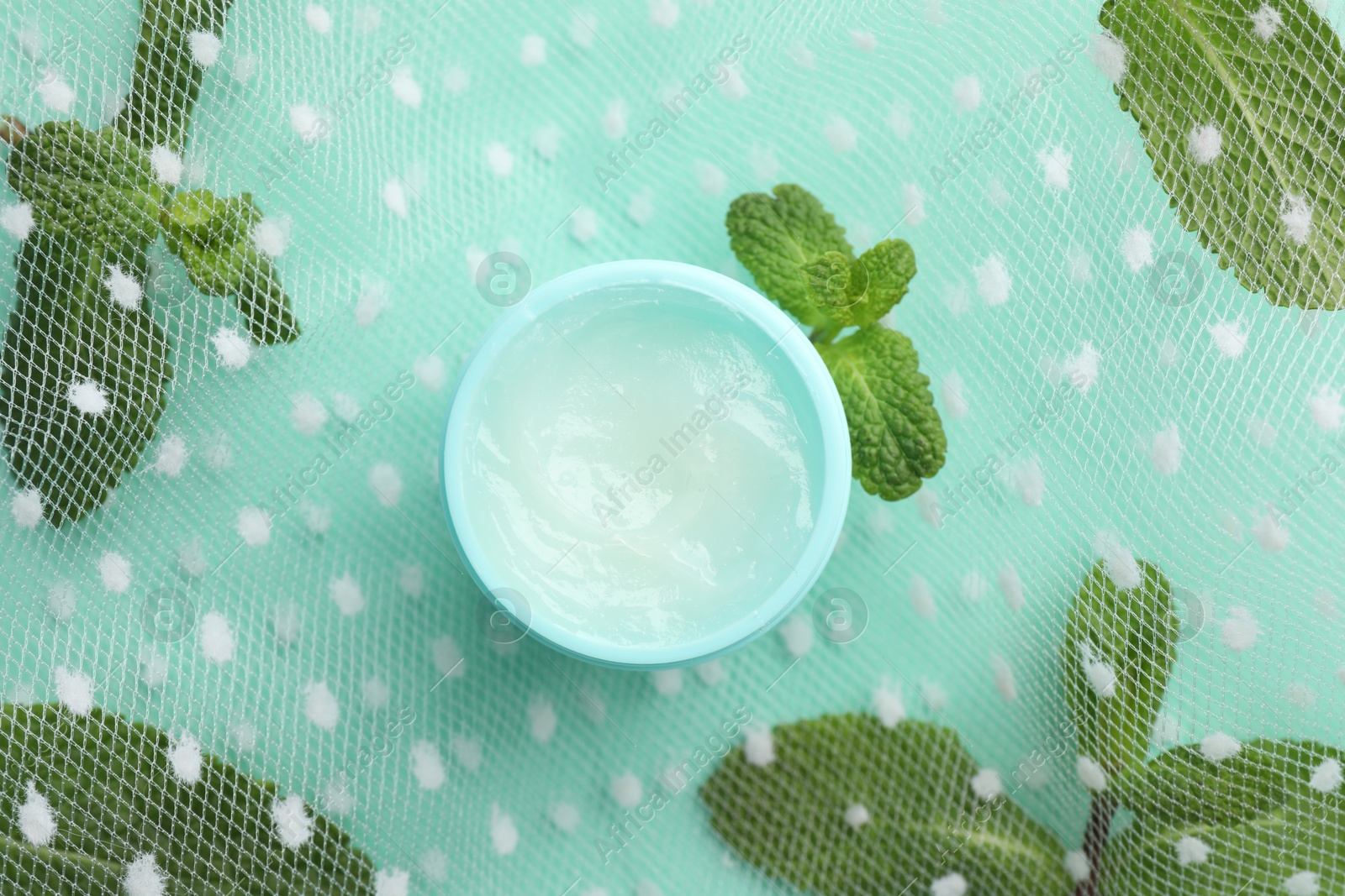 Photo of Natural lip balm, mint leaves and fabric on turquoise background, top view