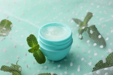 Photo of Natural lip balm, mint leaves and fabric on turquoise background, closeup