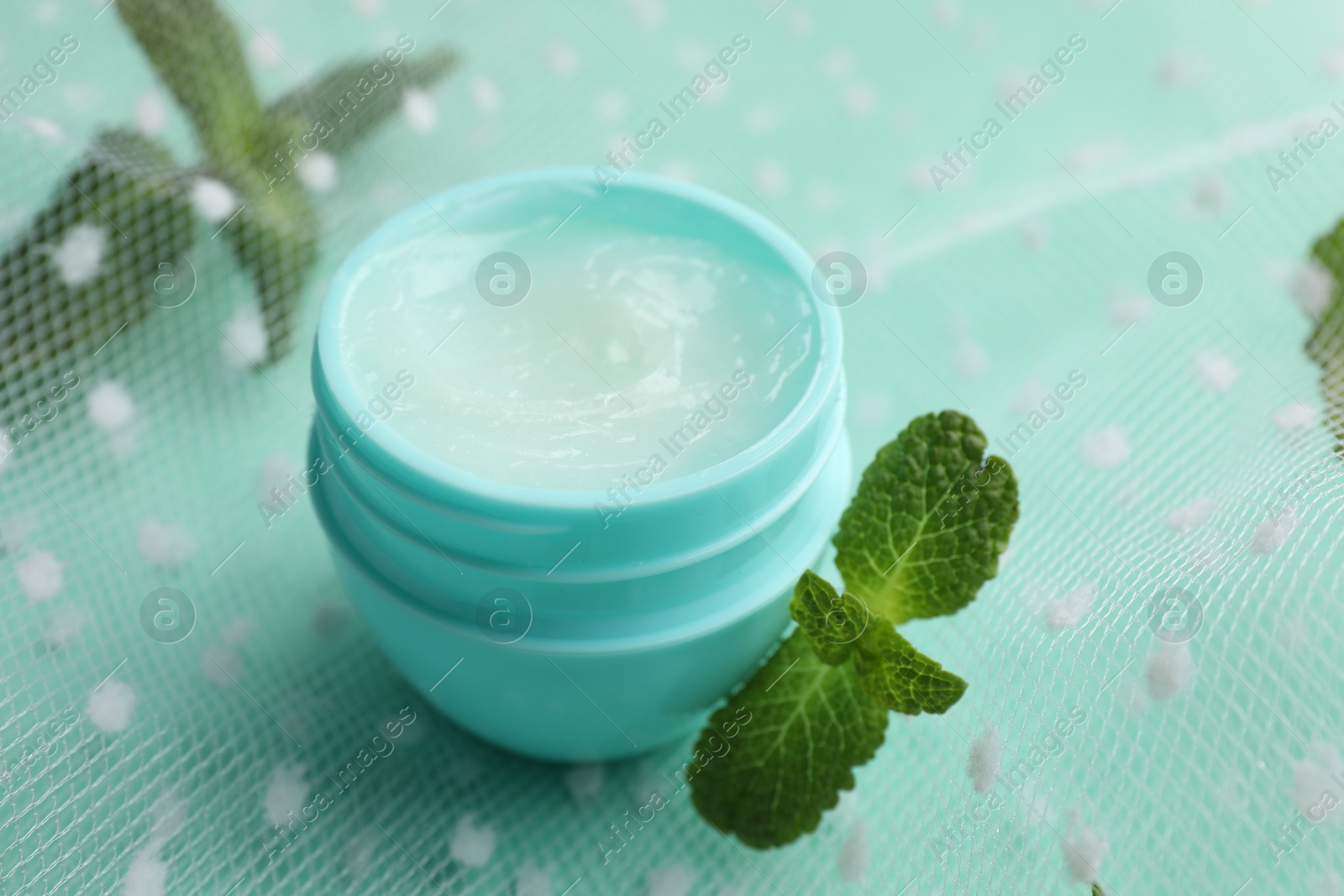 Photo of Natural lip balm, mint leaves and fabric on turquoise background, closeup