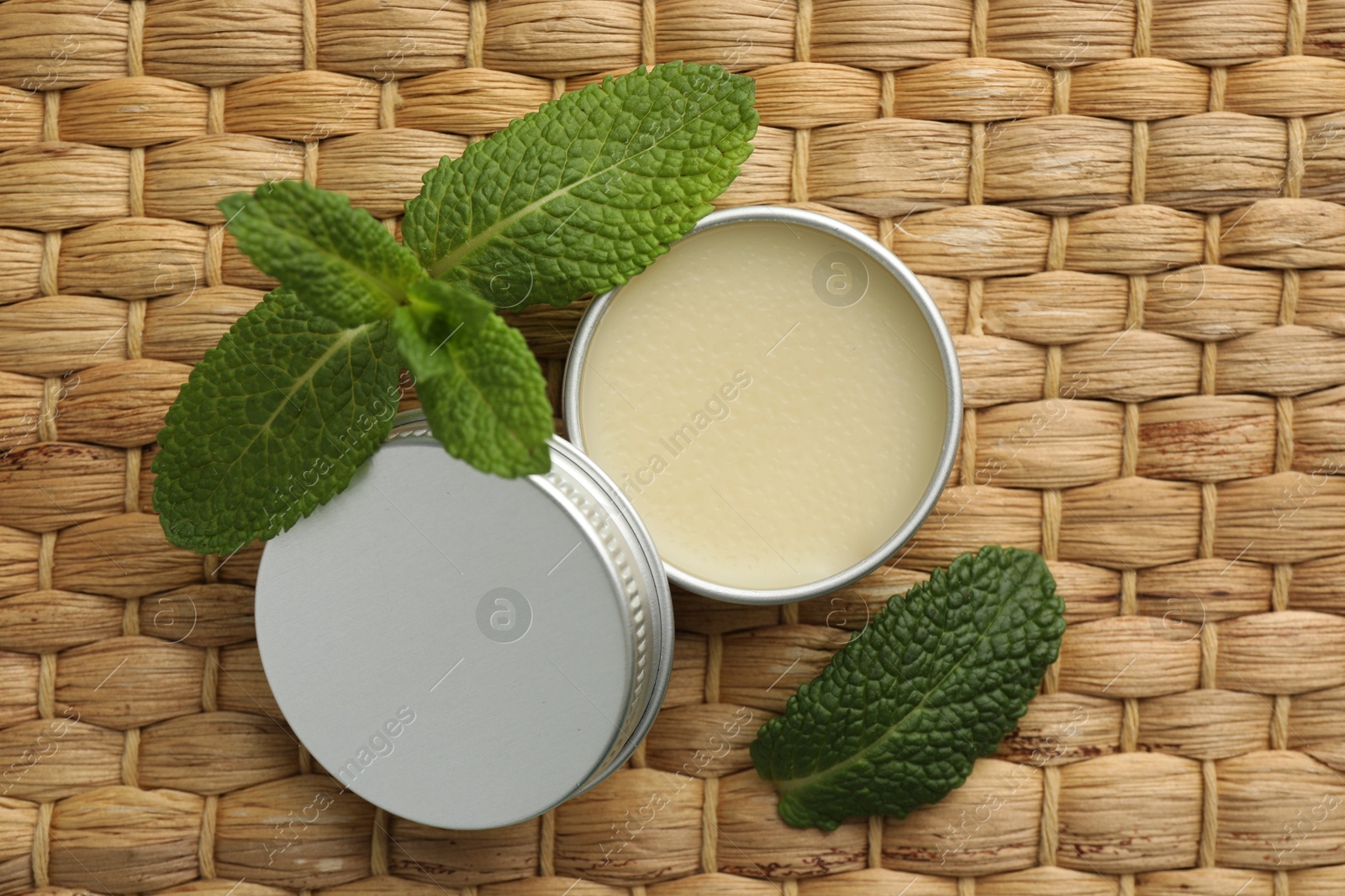 Photo of Natural lip balm and mint leaves on wicker background, top view