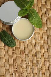 Photo of Natural lip balm and mint leaves on wicker background, top view. Space for text