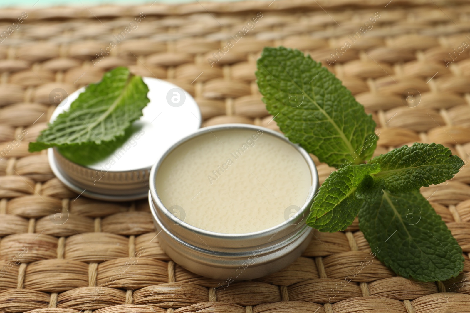 Photo of Natural lip balm and mint leaves on wicker background, closeup