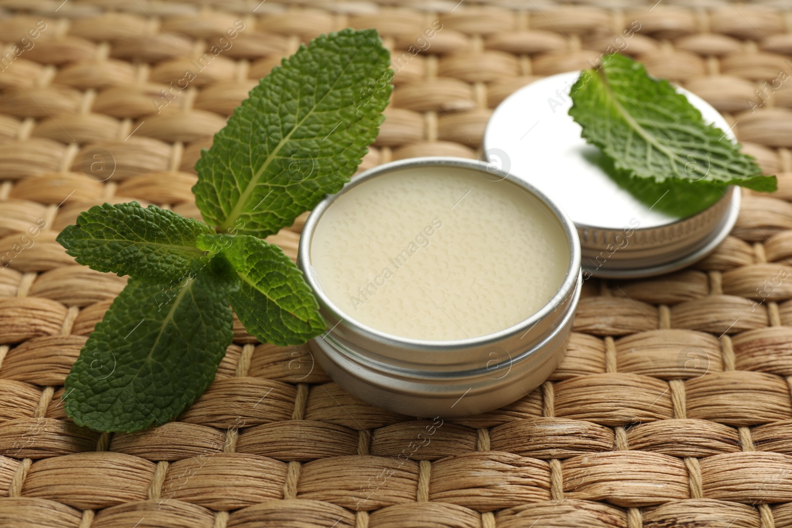 Photo of Natural lip balm and mint leaves on wicker background, closeup