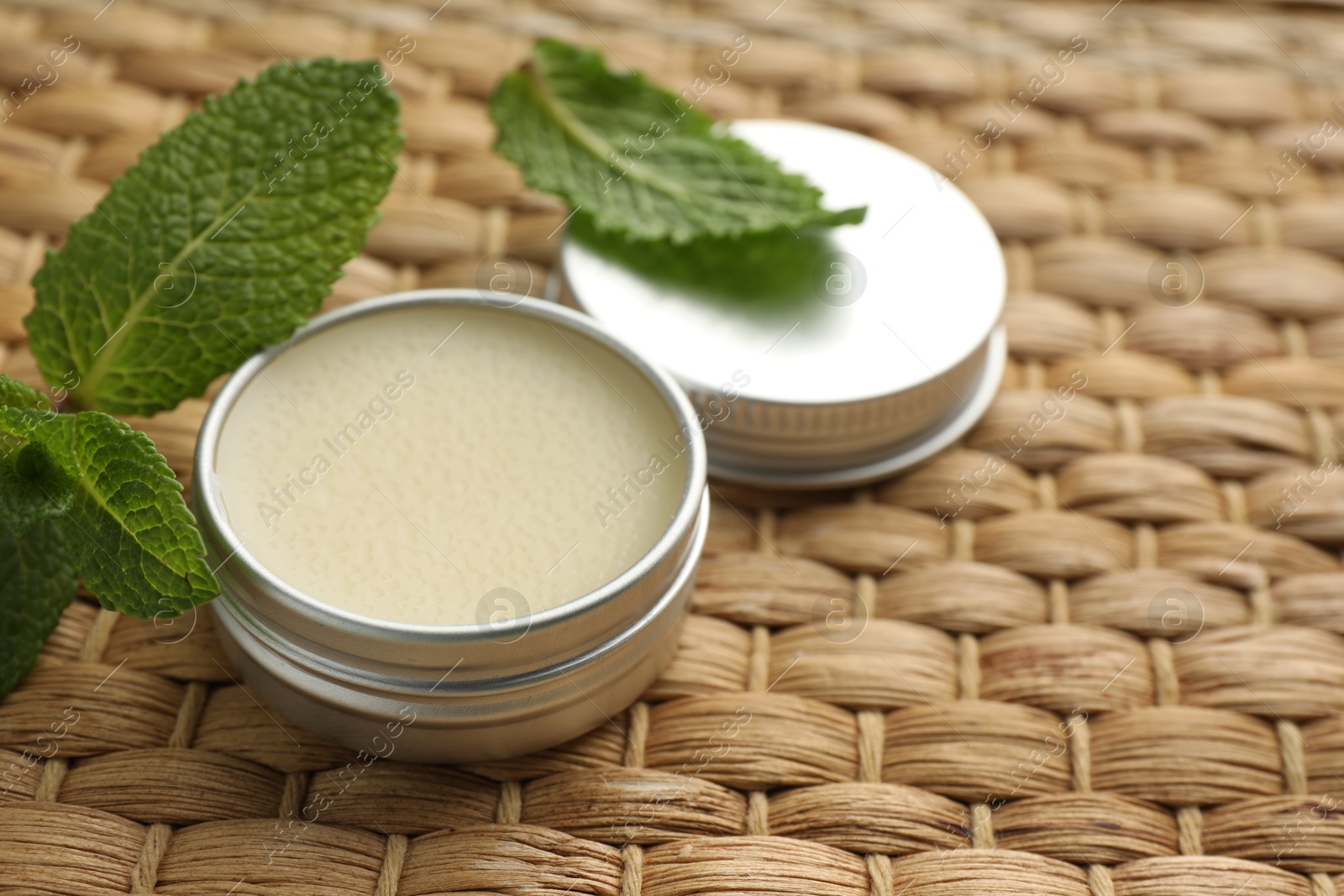 Photo of Natural lip balm and mint leaves on wicker background, closeup