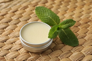 Photo of Natural lip balm and mint leaves on wicker background, closeup