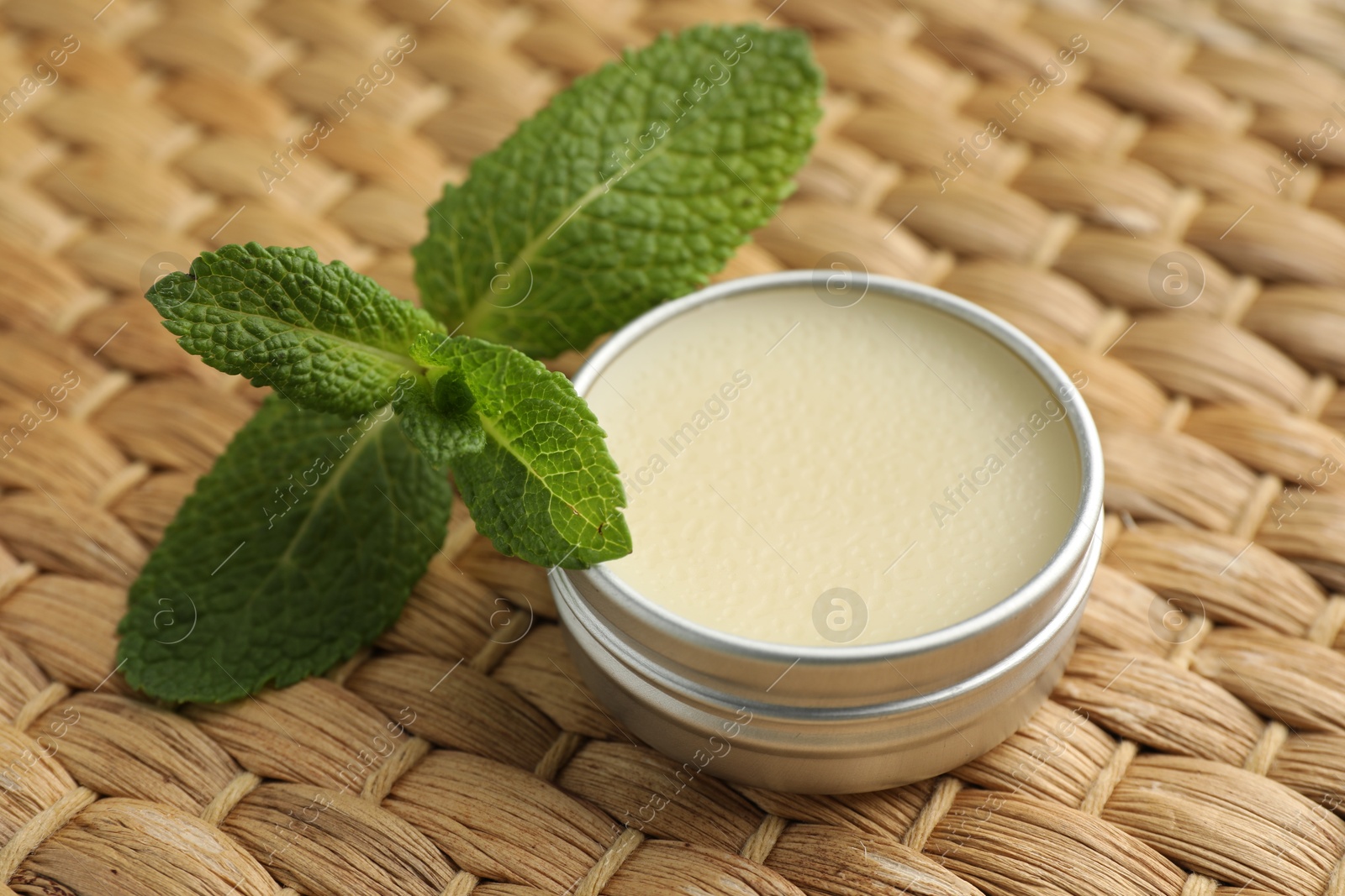 Photo of Natural lip balm and mint leaves on wicker background, closeup