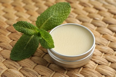 Photo of Natural lip balm and mint leaves on wicker background, closeup