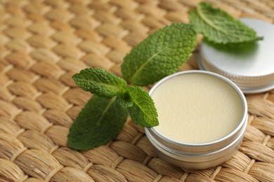 Photo of Natural lip balm and mint leaves on wicker background, closeup