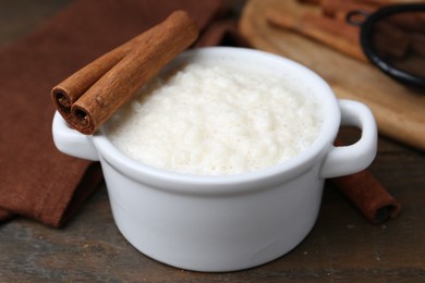 Photo of Delicious rice pudding with cinnamon sticks on wooden table, closeup