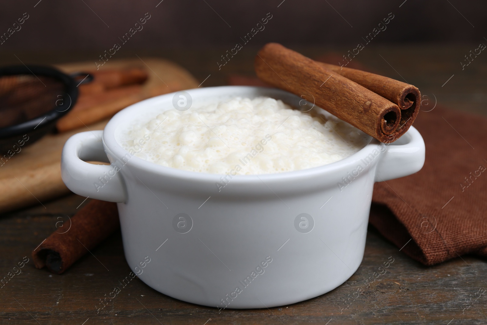 Photo of Delicious rice pudding with cinnamon sticks on wooden table, closeup