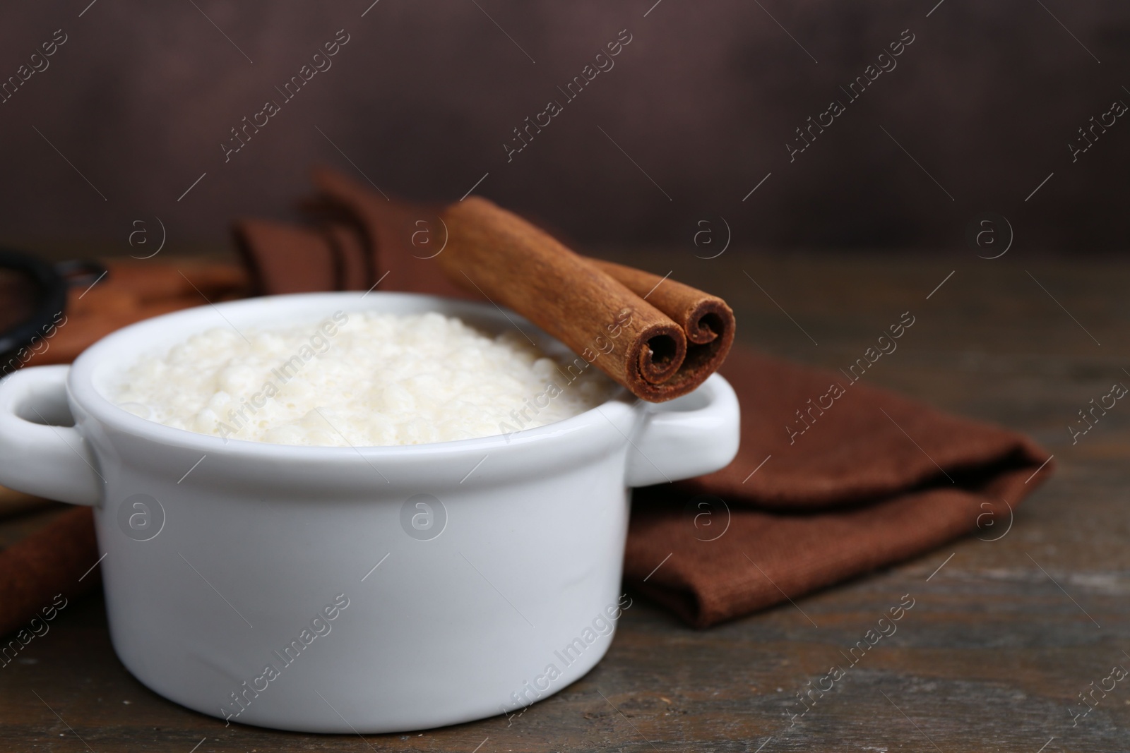 Photo of Delicious rice pudding with cinnamon sticks on wooden table, closeup. Space for text