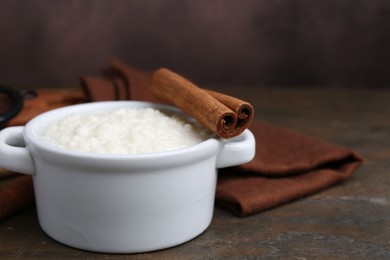 Photo of Delicious rice pudding with cinnamon sticks on wooden table, closeup. Space for text