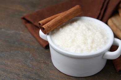 Photo of Delicious rice pudding with cinnamon sticks on wooden table, closeup