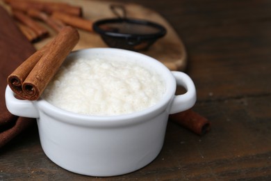 Photo of Delicious rice pudding with cinnamon sticks on wooden table, closeup