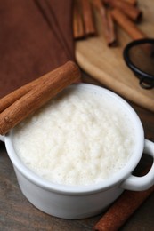 Photo of Delicious rice pudding with cinnamon sticks on wooden table, closeup