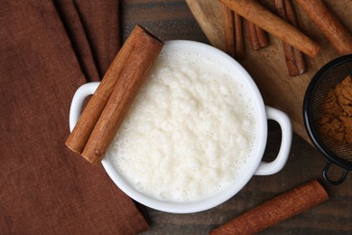 Photo of Delicious rice pudding with cinnamon sticks on wooden table, flat lay