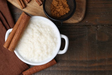 Photo of Delicious rice pudding with cinnamon sticks on wooden table, flat lay. Space for text