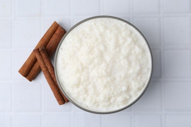 Photo of Delicious rice pudding with cinnamon sticks on white tiled table, top view