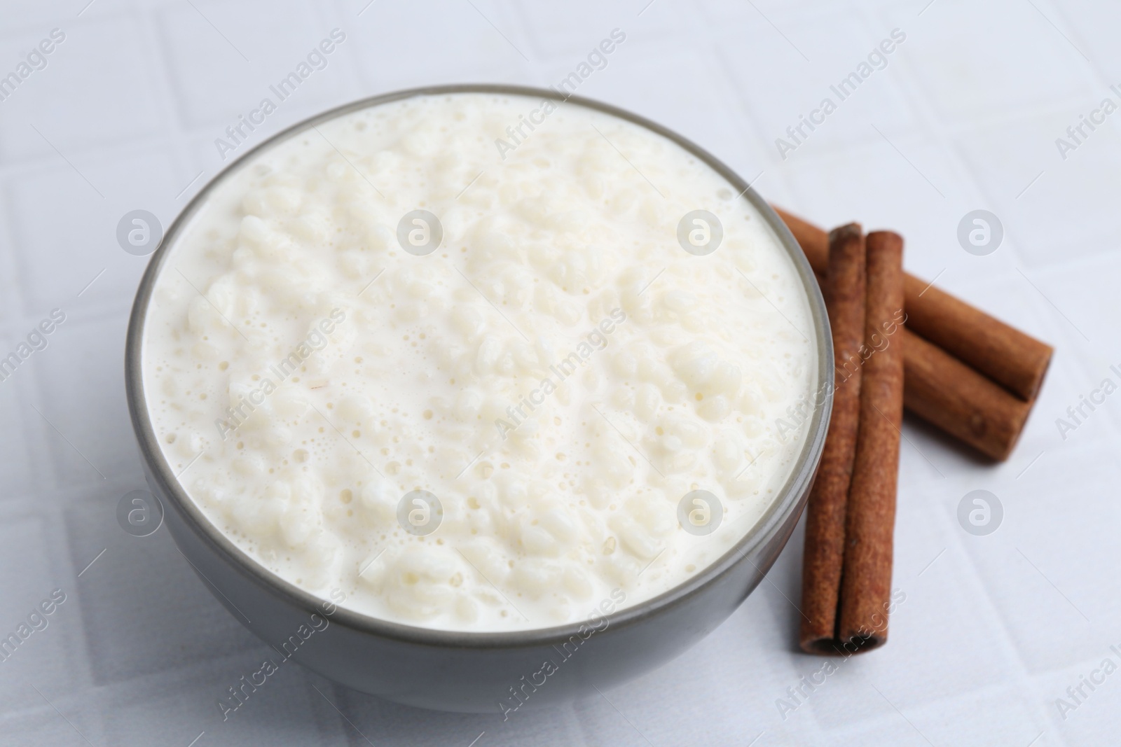 Photo of Delicious rice pudding with cinnamon sticks on white tiled table, closeup