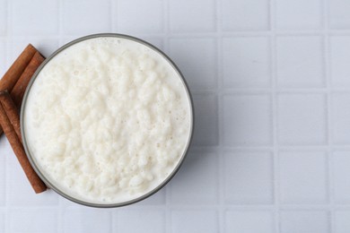 Photo of Delicious rice pudding with cinnamon sticks on white tiled table, top view. Space for text