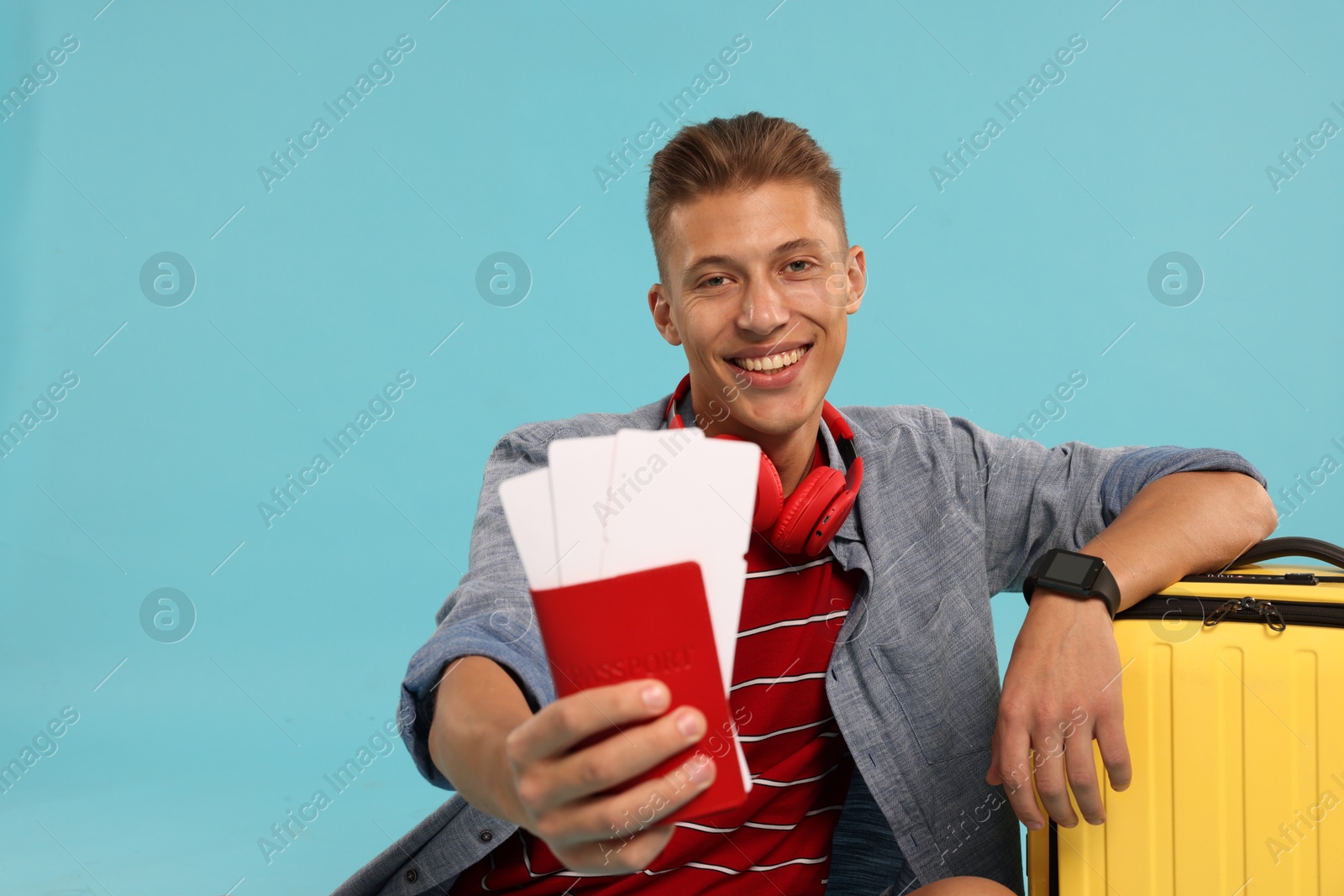 Photo of Happy traveller with suitcase, passport and tickets on light blue background