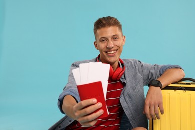 Photo of Happy traveller with suitcase, passport and tickets on light blue background