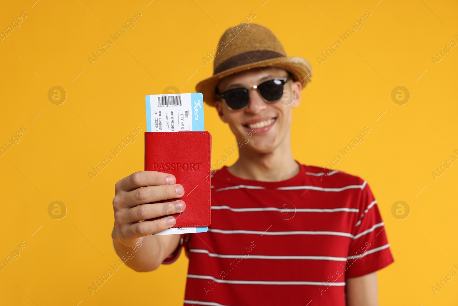 Photo of Happy traveller in sunglasses with passport and ticket on yellow background, selective focus