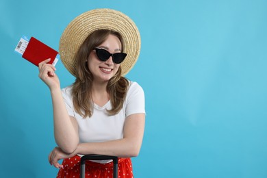 Photo of Happy traveller in sunglasses with suitcase, passport and ticket on light blue background, space for text