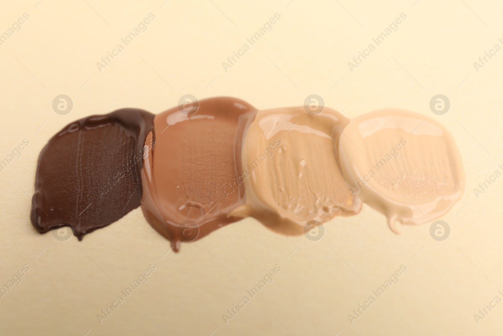 Photo of Samples of different foundations on beige background, closeup