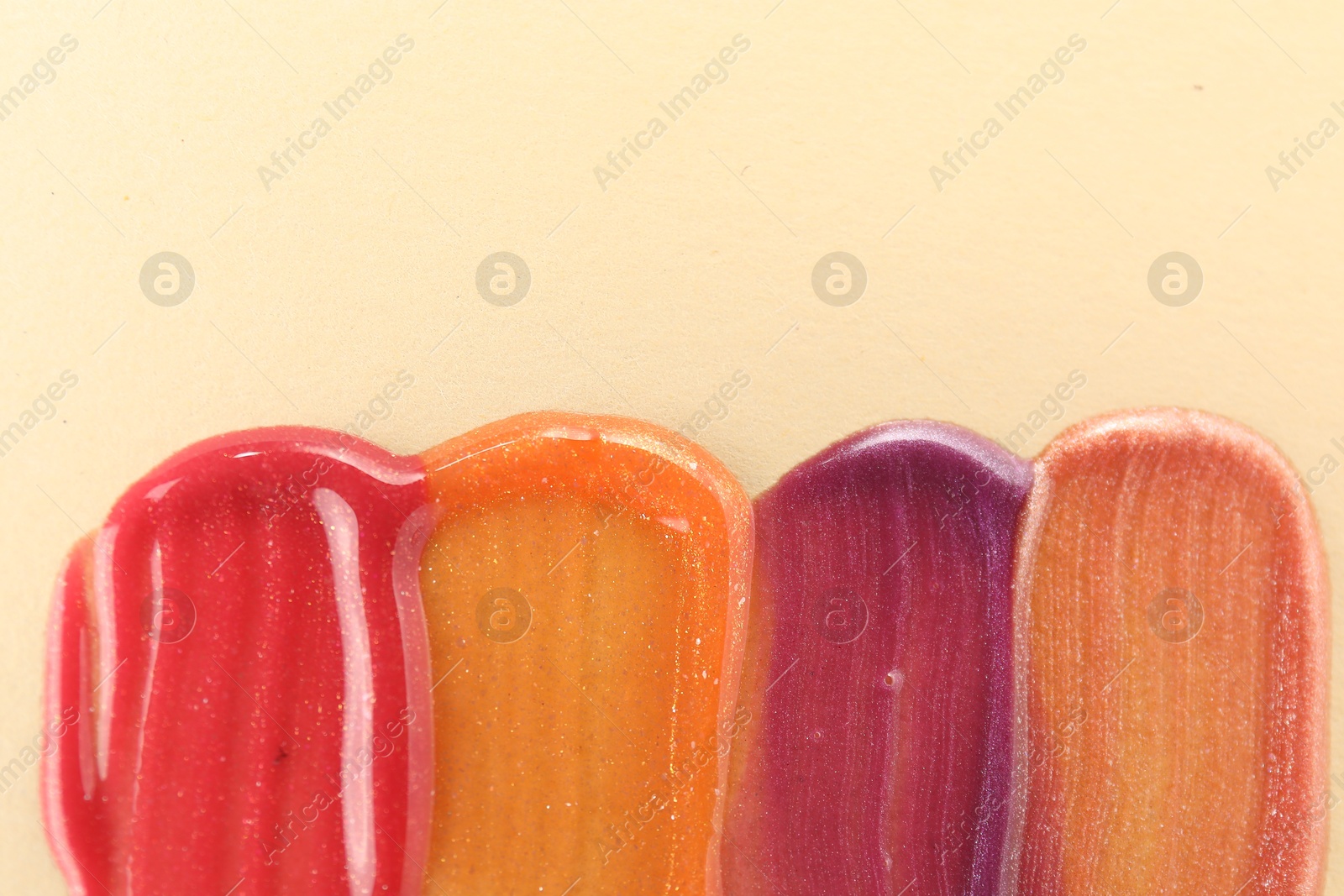 Photo of Samples of different lipglosses on beige background, top view. Space for text