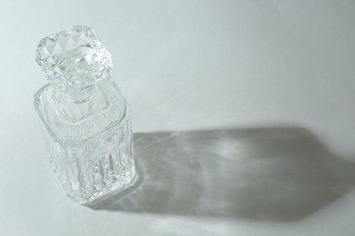 Photo of Beautiful crystal bottle casting shadow on light background. Space for text