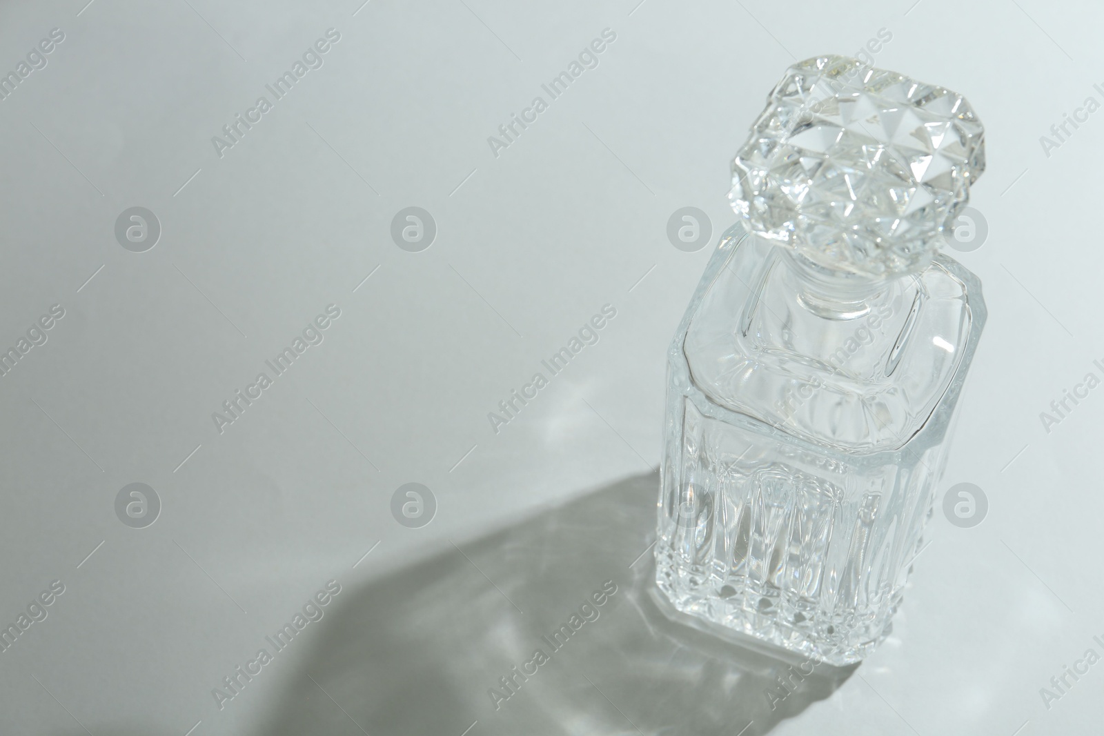 Photo of Beautiful crystal bottle casting shadow on light background. Space for text