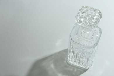 Photo of Beautiful crystal bottle casting shadow on light background. Space for text