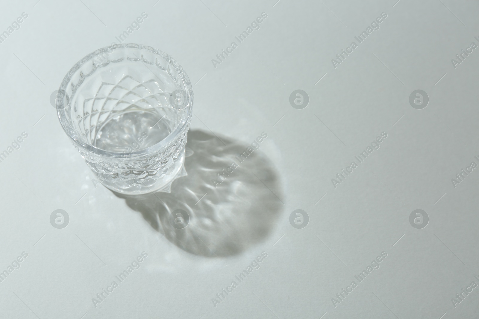 Photo of Beautiful crystal glass casting shadow on light background. Space for text