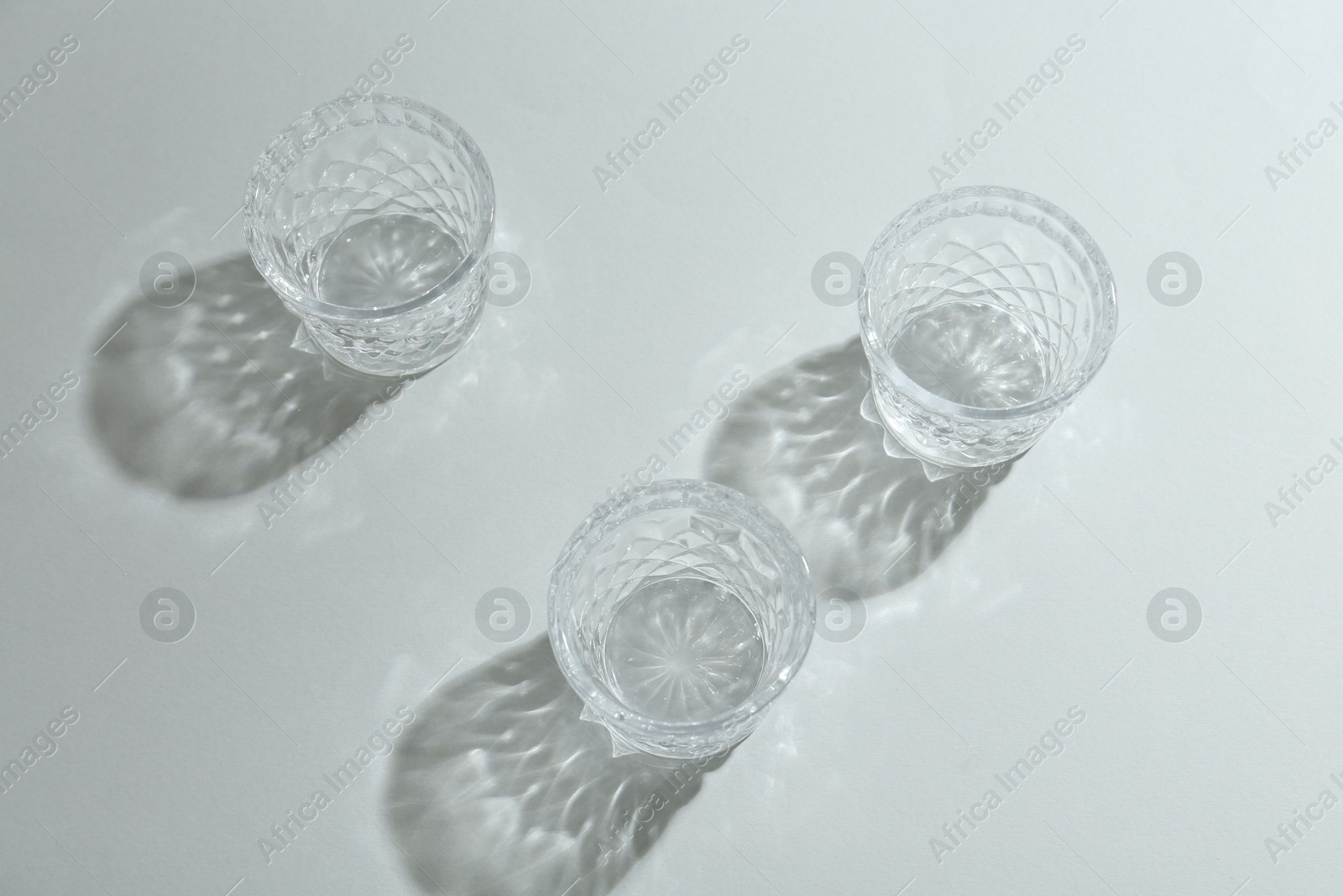 Photo of Beautiful crystal glasses casting shadows on light background, above view