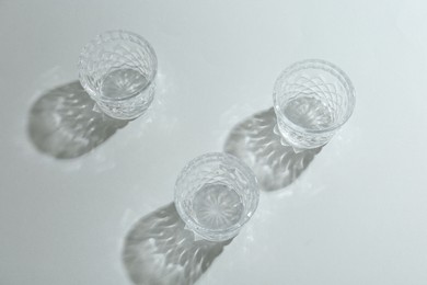 Photo of Beautiful crystal glasses casting shadows on light background, above view