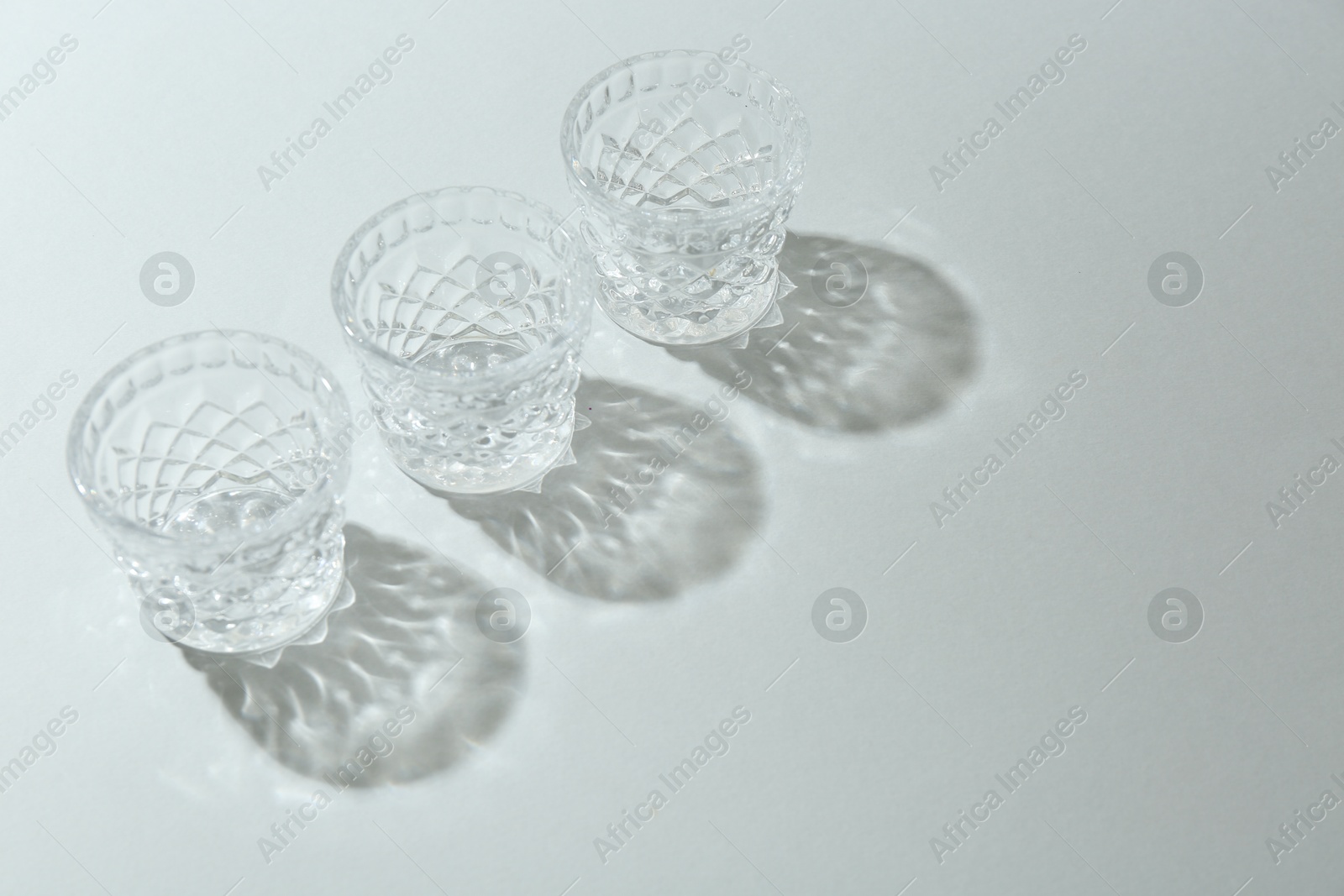 Photo of Beautiful crystal glasses casting shadows on light background