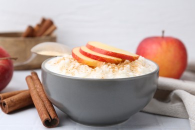 Photo of Delicious rice pudding with apples and cinnamon on white tiled table, closeup