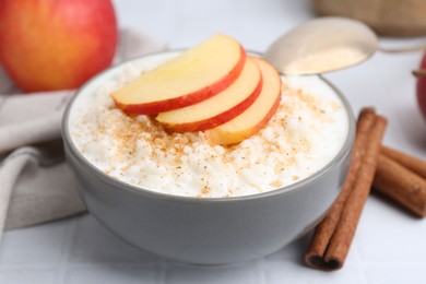 Photo of Delicious rice pudding with apples and cinnamon on white tiled table, closeup